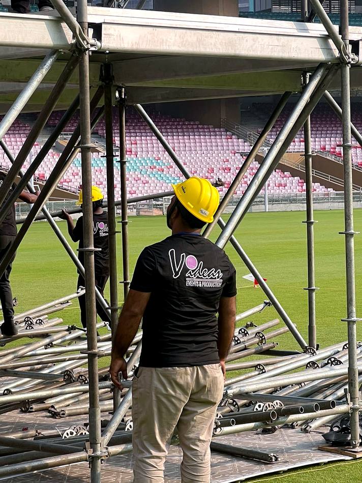 VIDEAS crew member in branded shirt and helmet inspecting scaffolding build at DY Patil Stadium